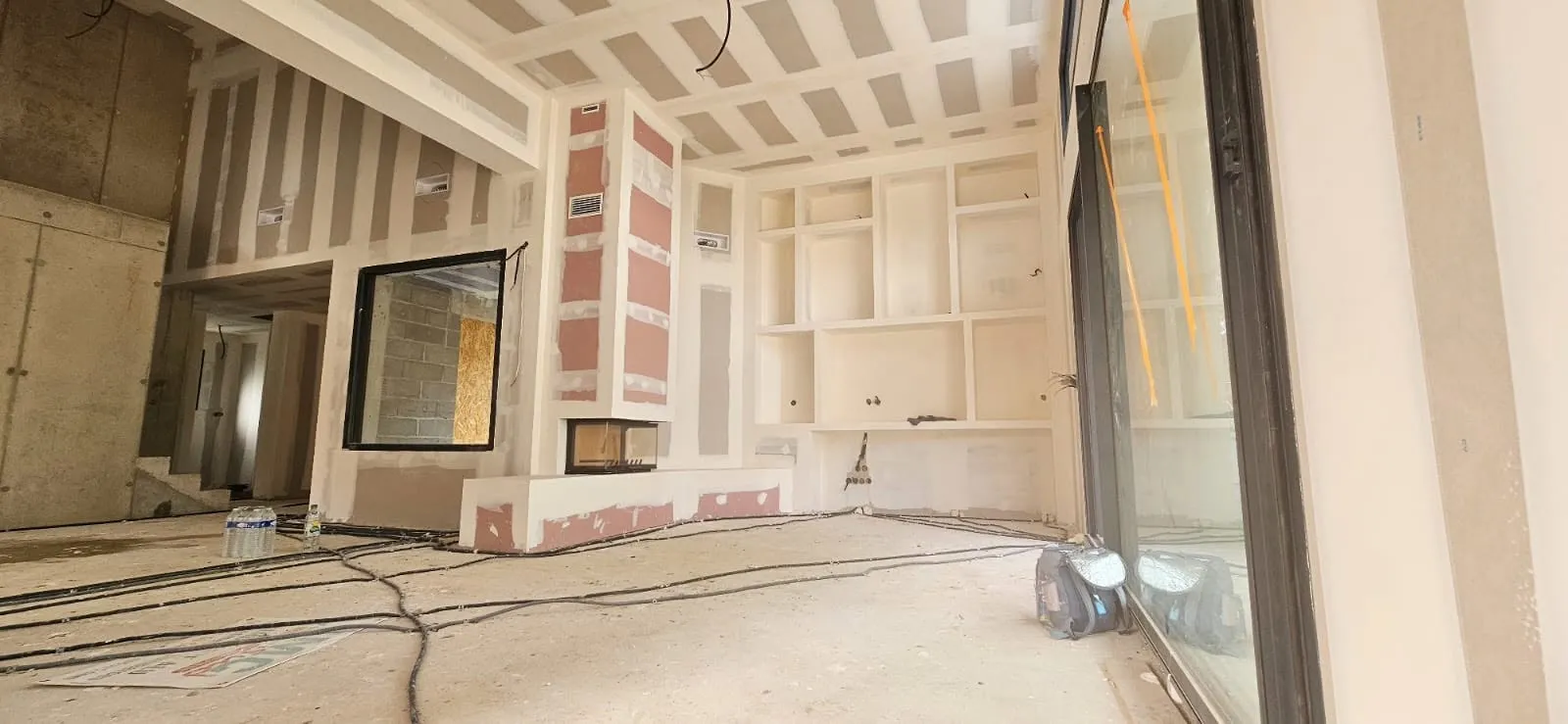 Grande pièce en chantier avec plaques de plâtre jointoyées et poutres en bois apparentes