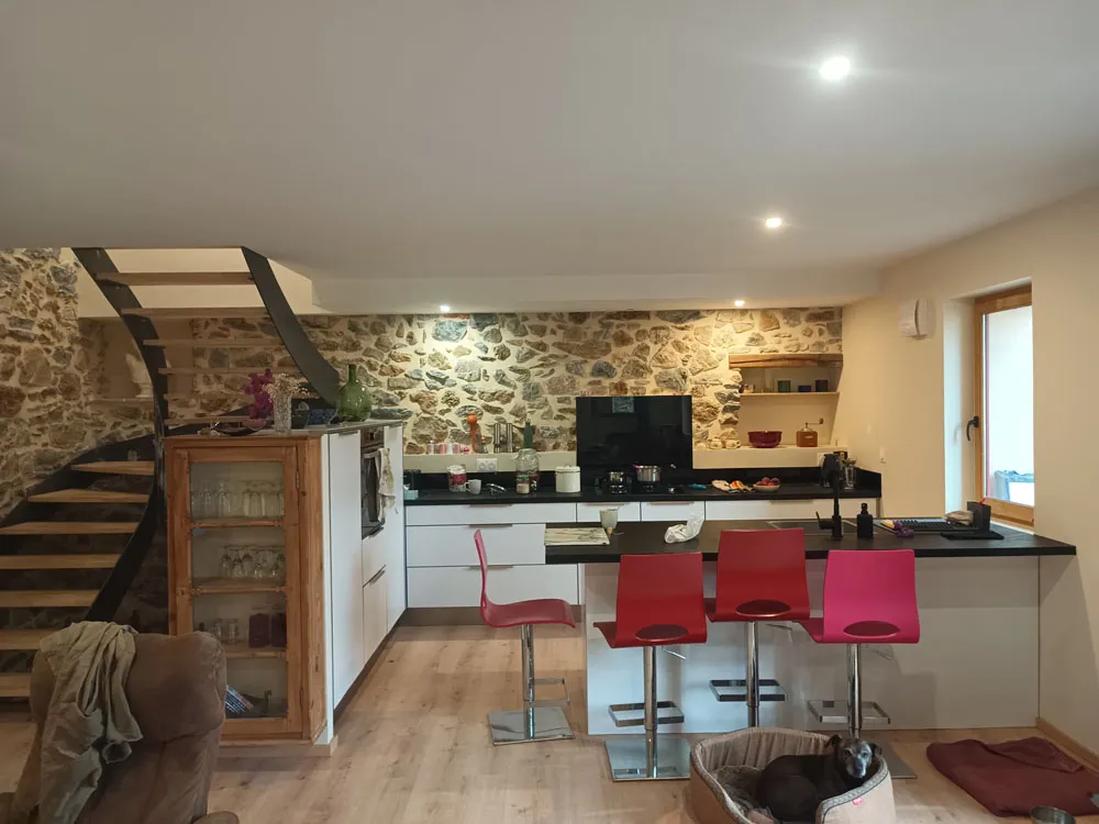 Cuisine ouverte rénovée avec plafond lisse, mur en pierre apparente et escalier métallique