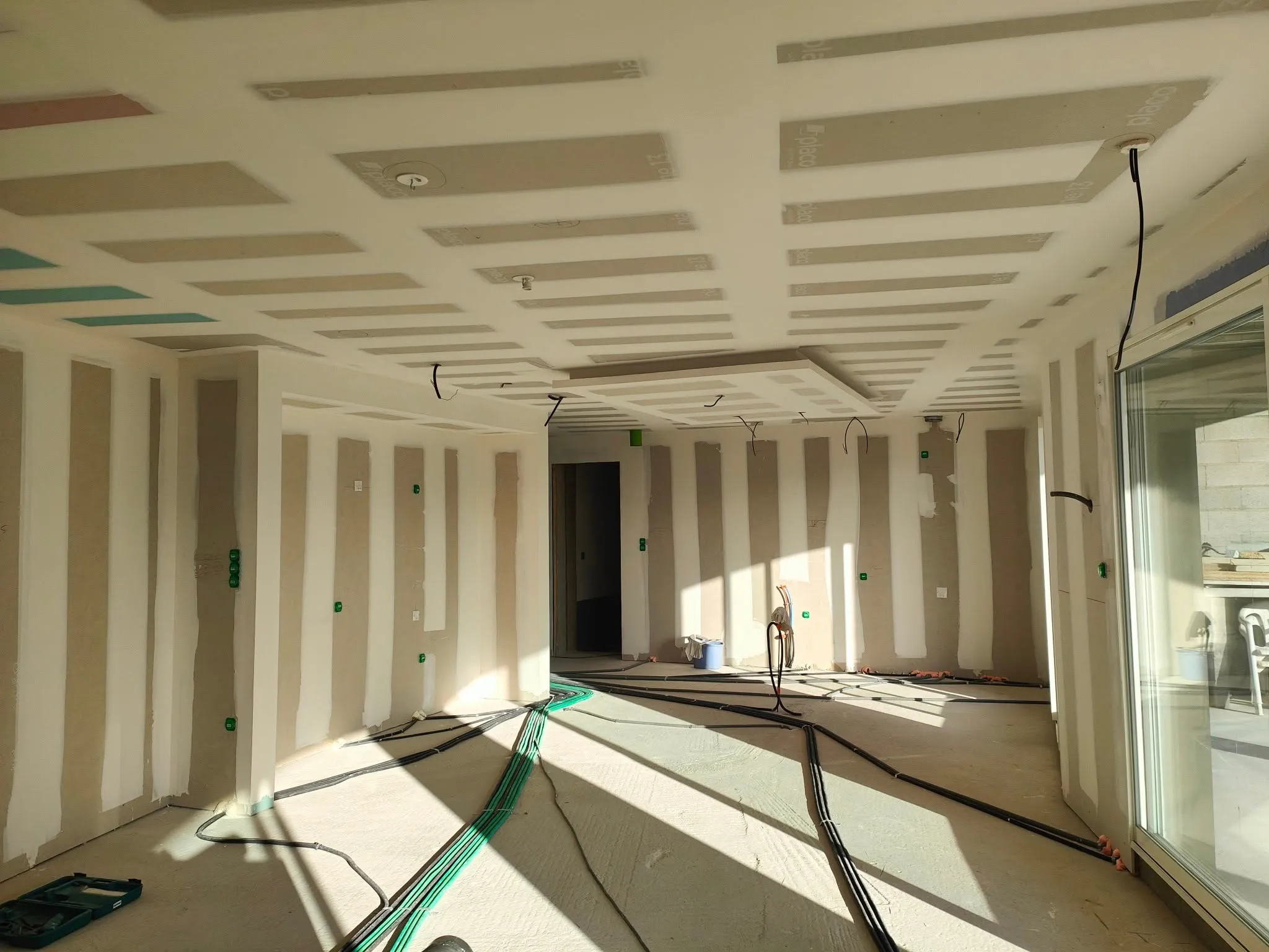 Plafond et cloisons en plaques de plâtre en cours de jointoiement dans le séjour d'une maison neuve, chantier de plaquiste UF Plaquiste.