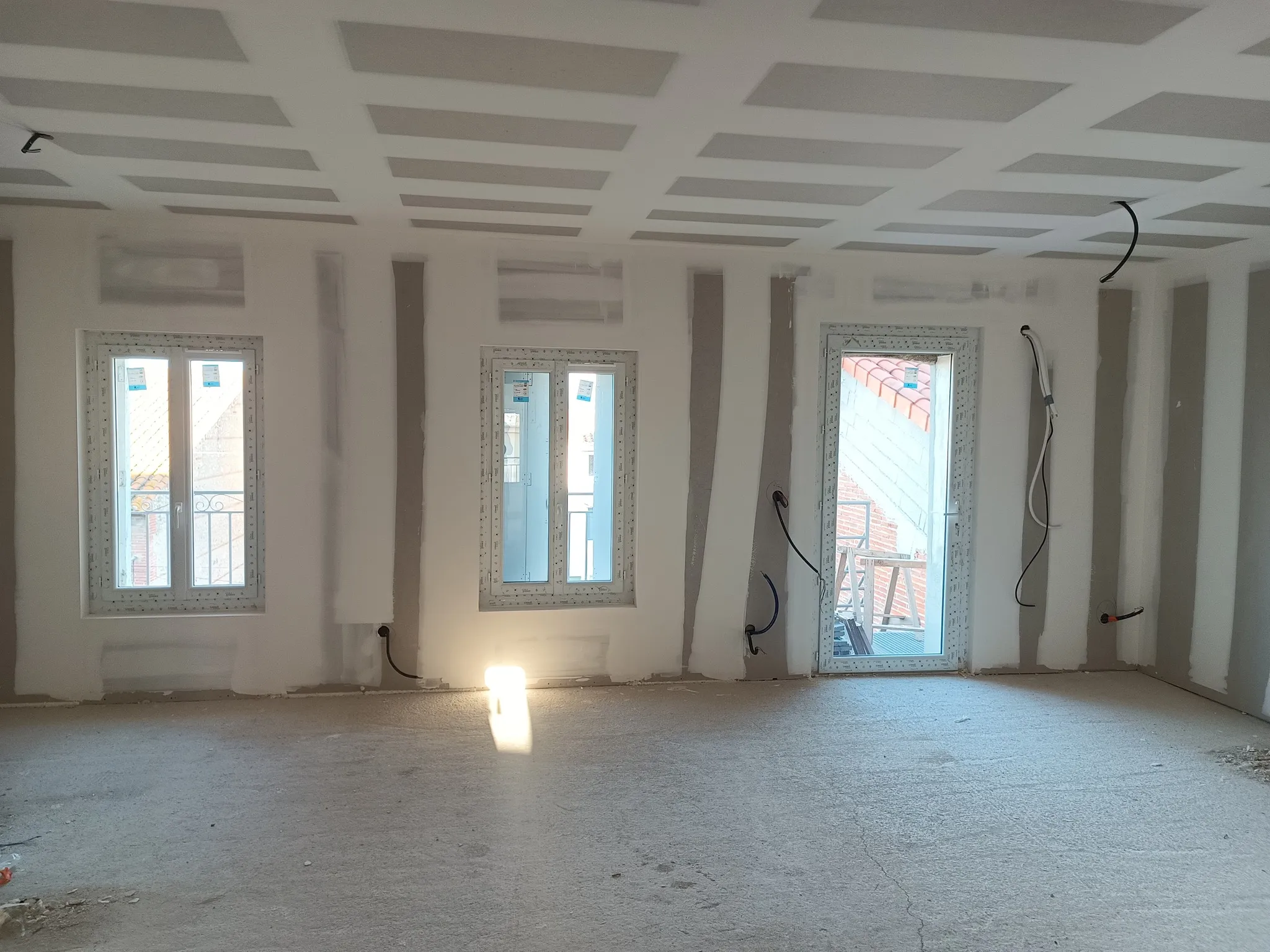 Grande pièce avec trois ouvertures, plafond en plaques de plâtre et murs en cours de joints