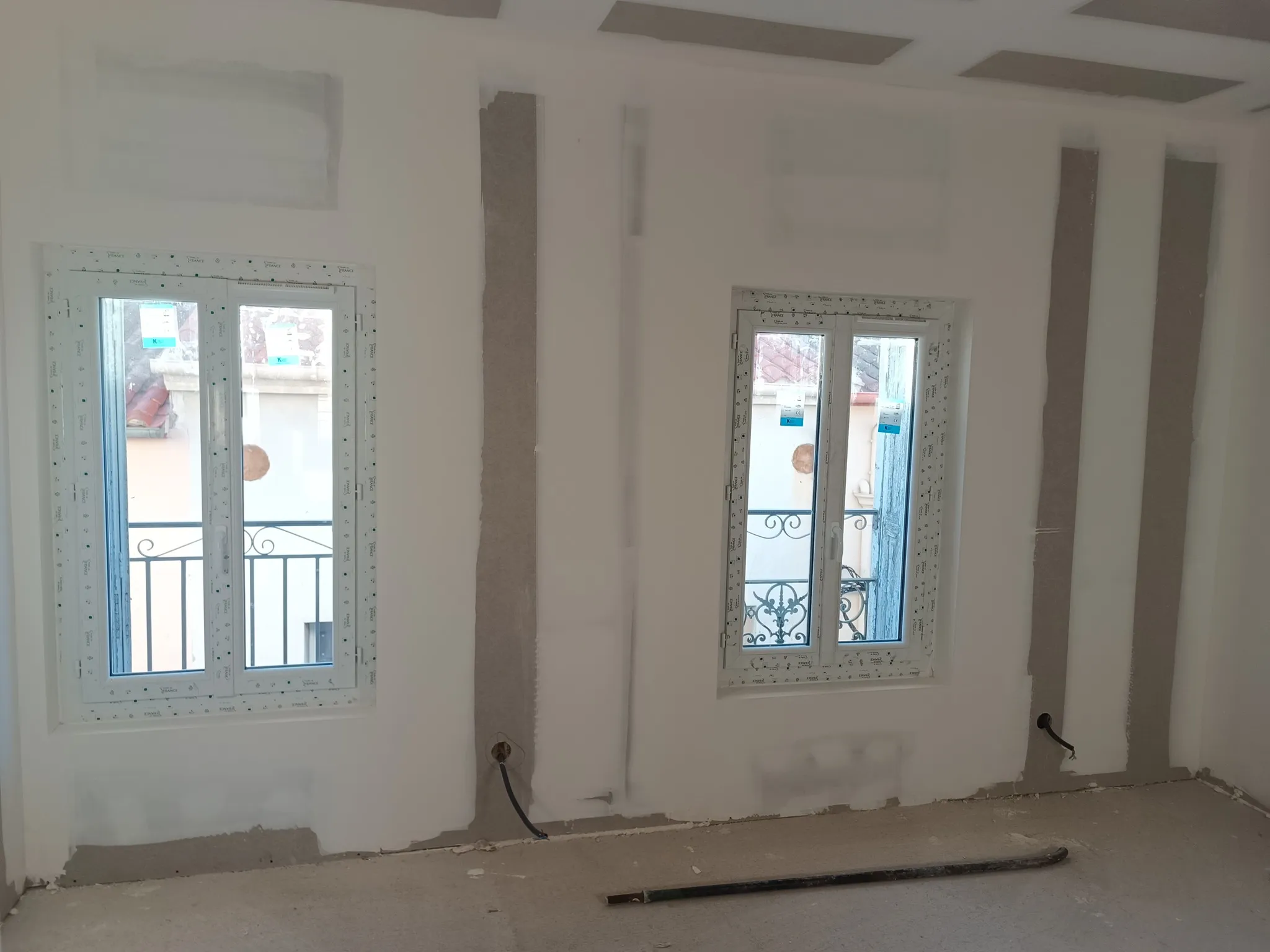 Pièce avec deux fenêtres neuves aux montants jointoyés et garde-corps en fer forgé visibles dehors